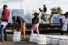 People grab packs of water bottles from a truck bed.