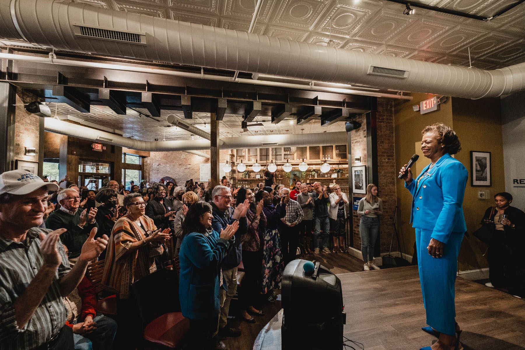 People clap for Cheri Beasley as she smiles from a stage at a community meeting at Beyu Caffe.