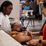 Midwife Angie Miller listens to a baby's heartbeat while speaking to her client and her partner.