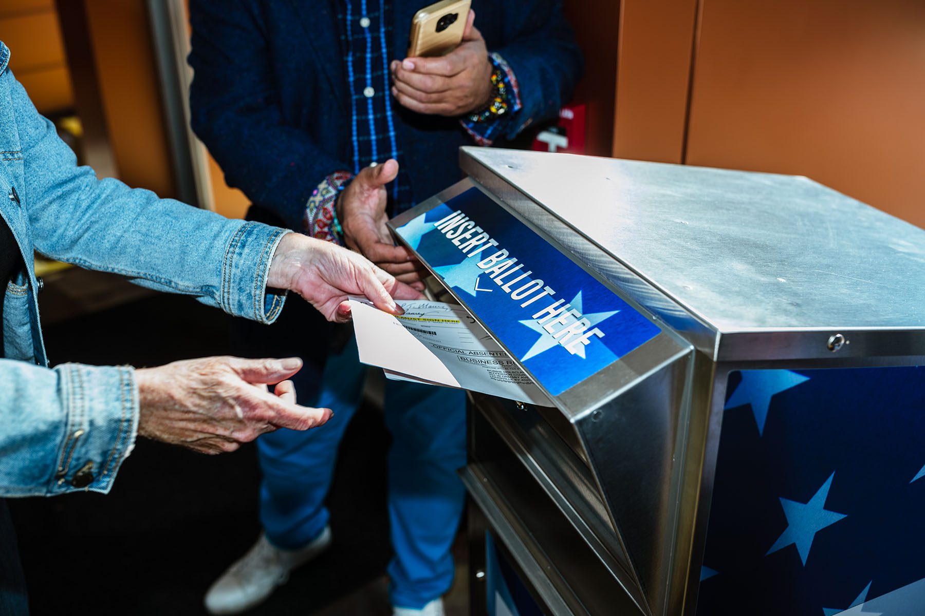 A person delivers their absentee ballot into a ballot drop.