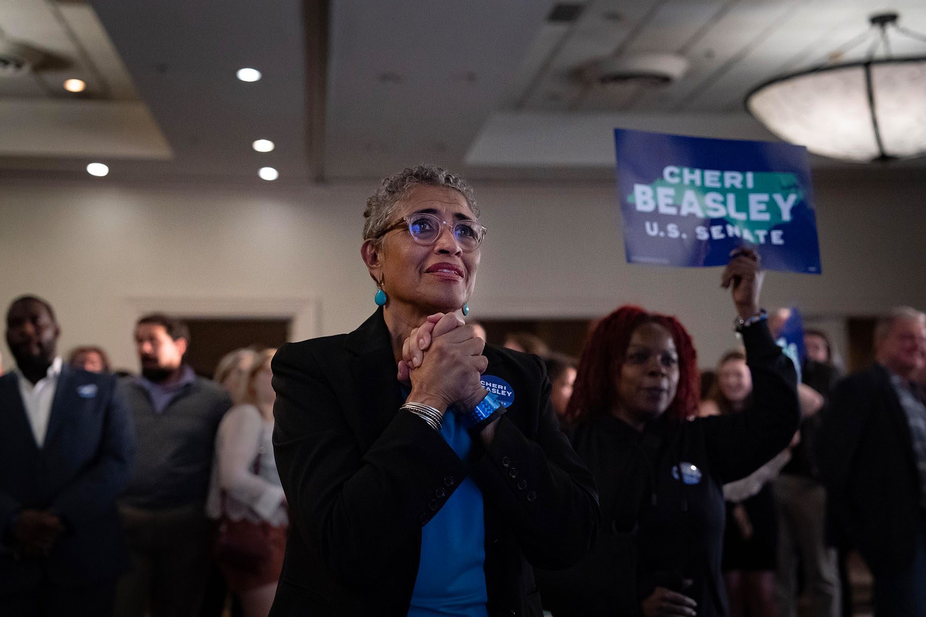 A woman clenches her hands and watches screens worryingly at an election night party.