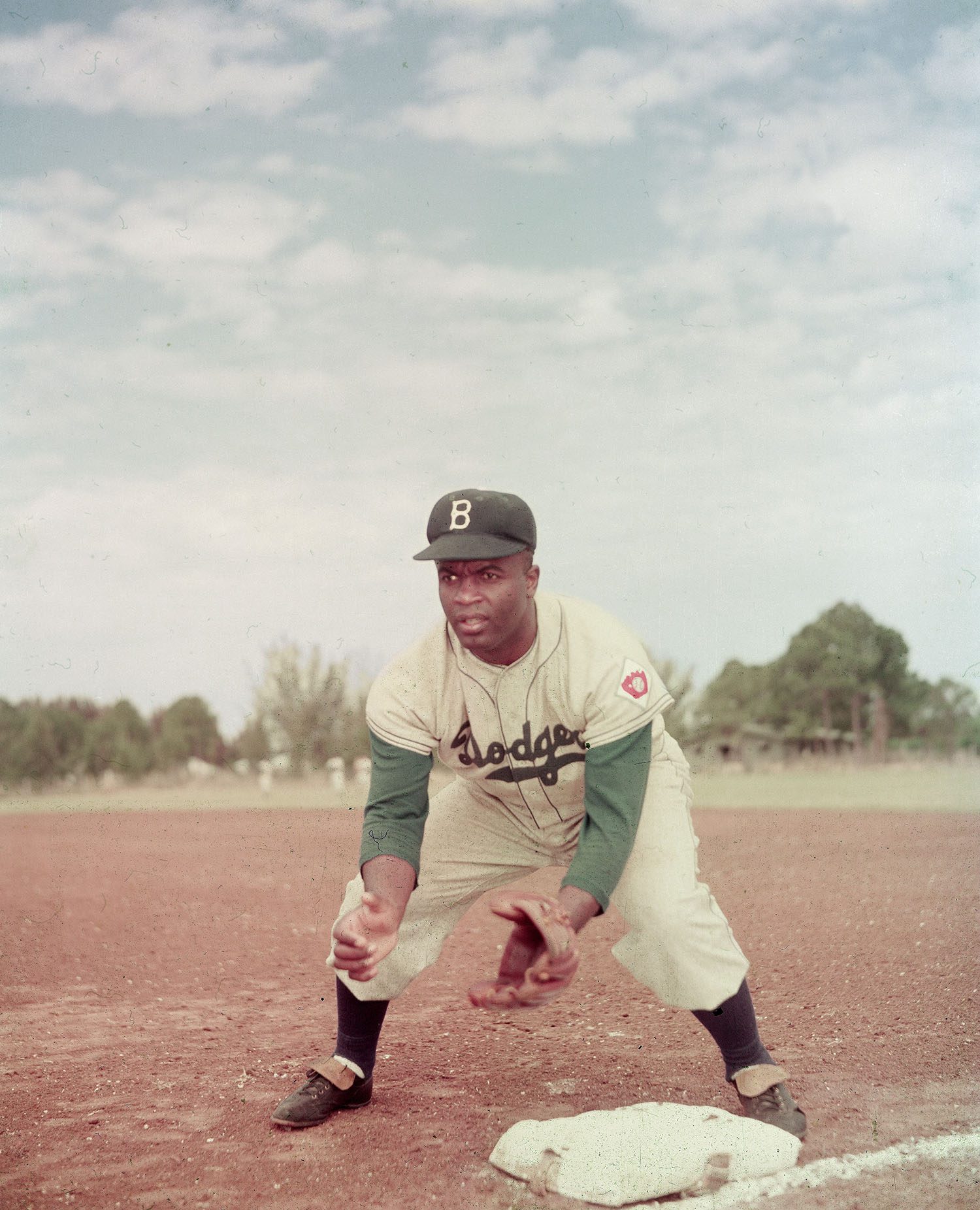 Jackie Robinson of the Brooklyn Dodgers crouches by the base and prepares to catch a ball in 1951