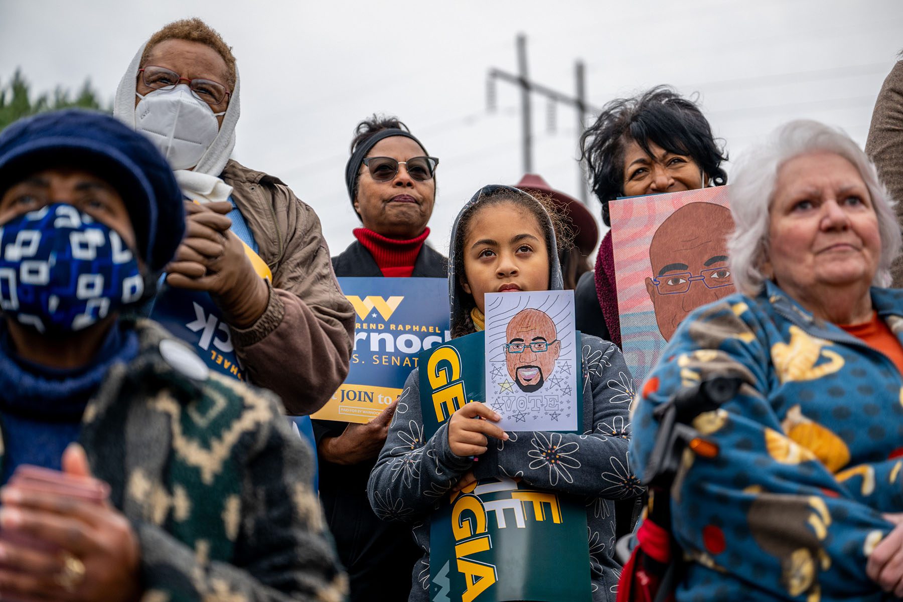 Supporters hold up signs and drawings of Sen. Raphael Warnock as he speaks during a campaign rally.