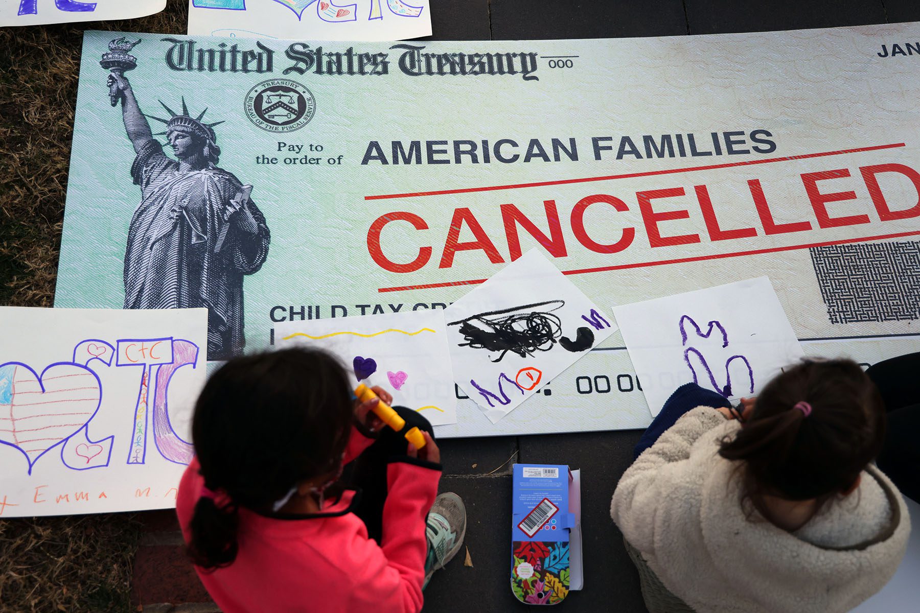 Children draw on top of a "canceled check" prop during a rally calling for the extension of the expanded Child Tax Credit.