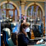 Rep. Julie McCluskie wears a face mask and is surrounded by protective plastic barriers reflecting the names of Colorado representatives from the monitor on the wall in the House chambers at the Colorado State Capitol during an emergency legislative session.