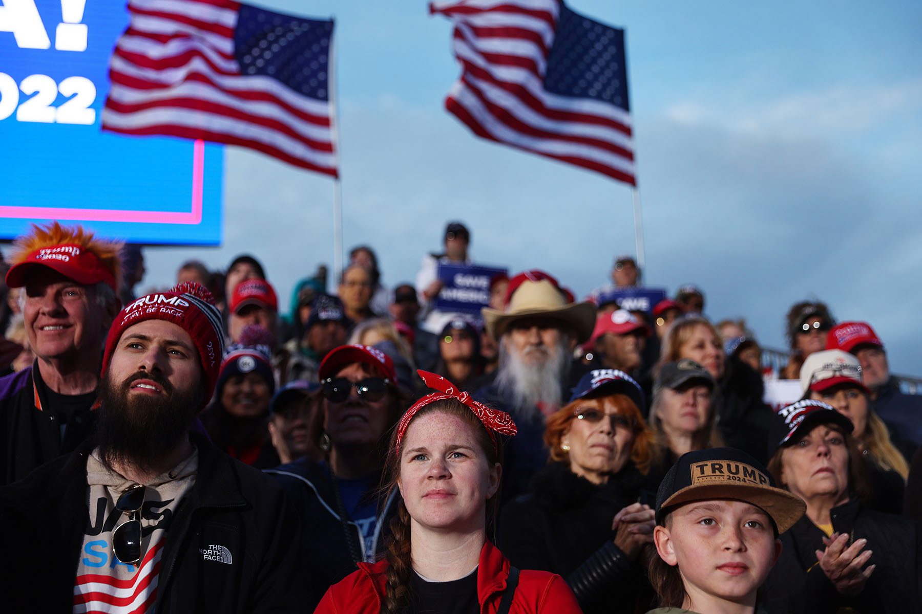 Trump supporters wearing "Trump 2024" hats gather at a rally.