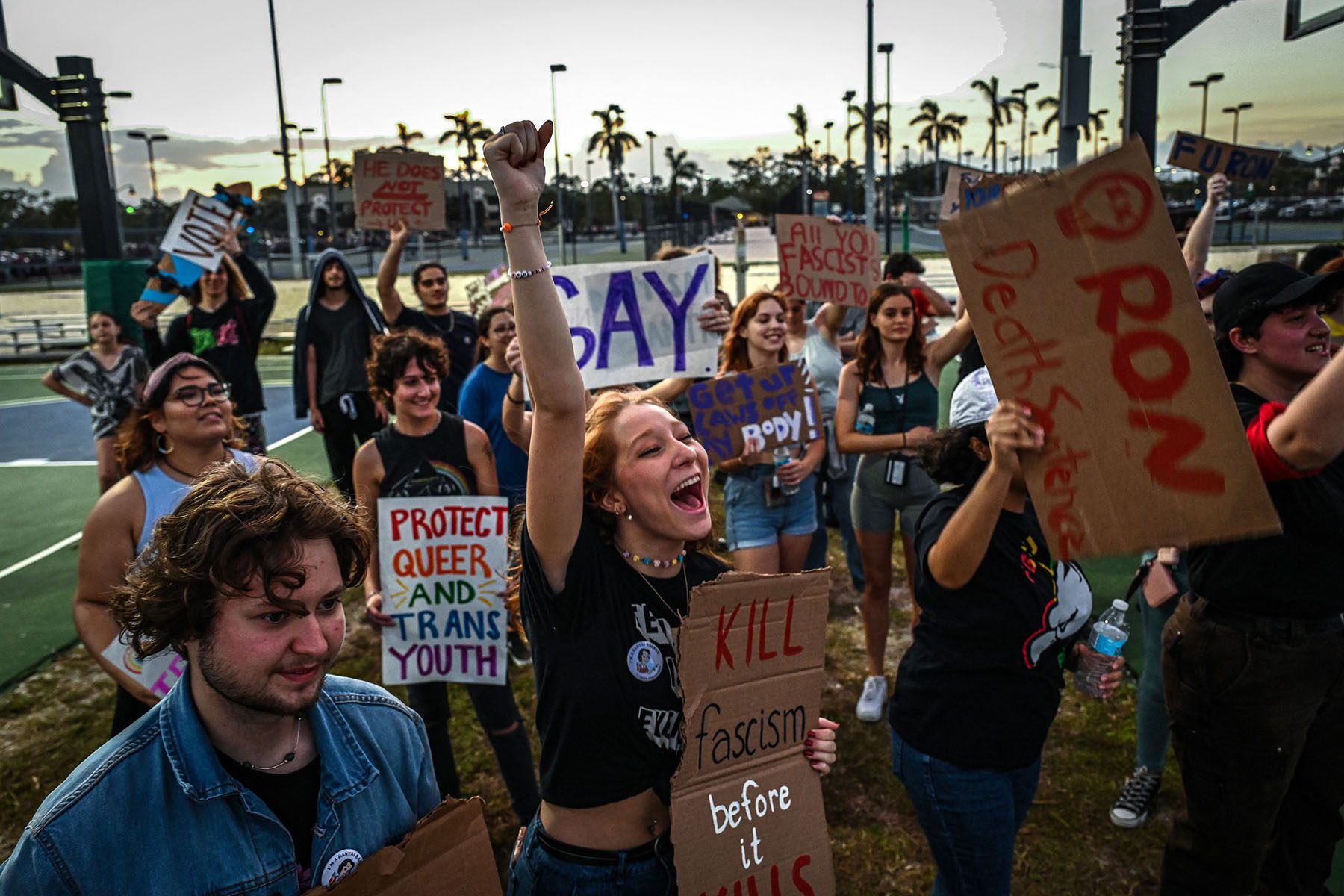 Demonstrators hold signs in support of queer youth outside a Ron DeSantis campaign event.