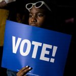 A supporter holds a blue sign that reads 