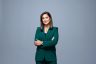 Headshot of Amna Nawaz crossing her arms and smiling in a green suit over a grey background..