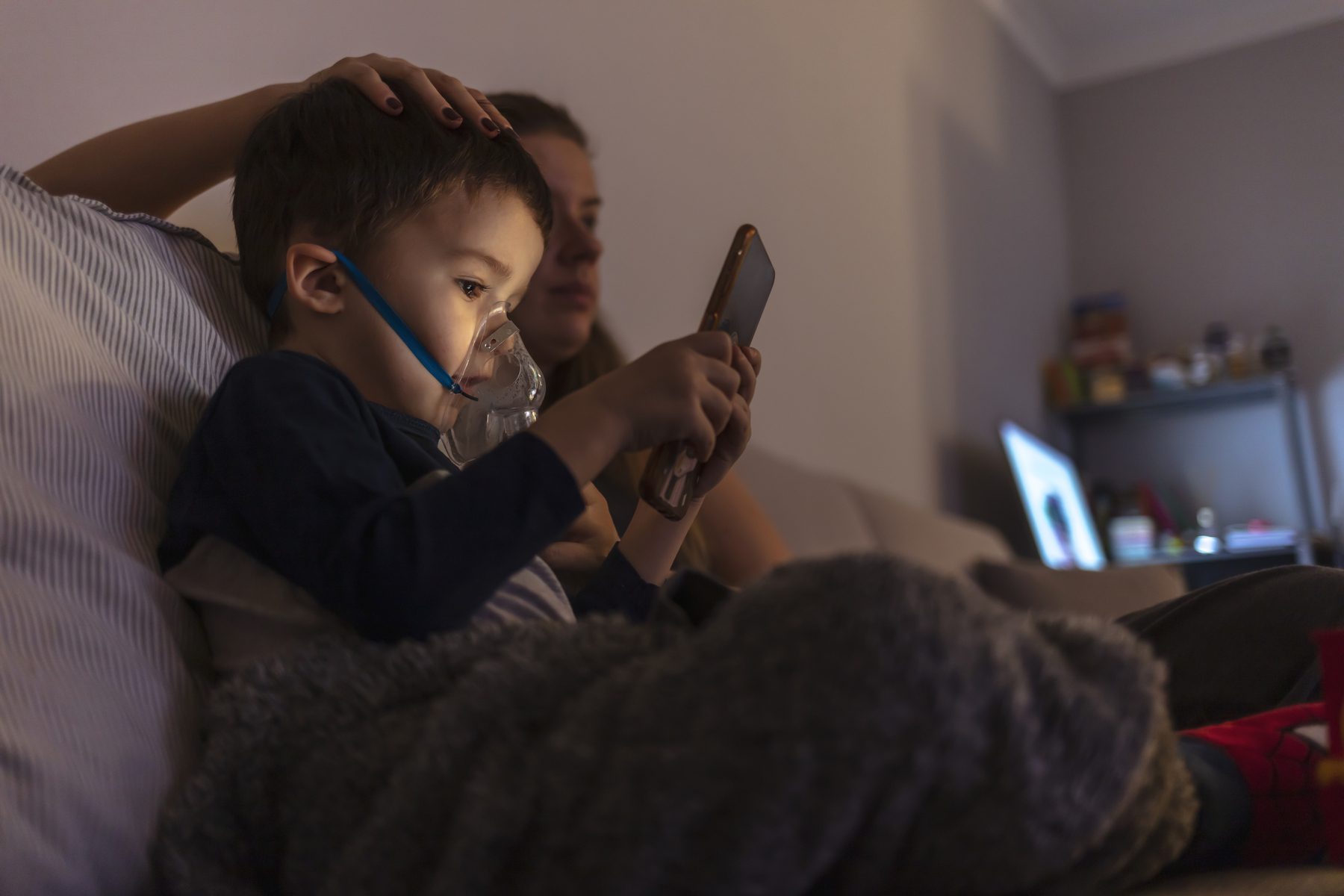 A mother helps a boy use a nebulizer machine.