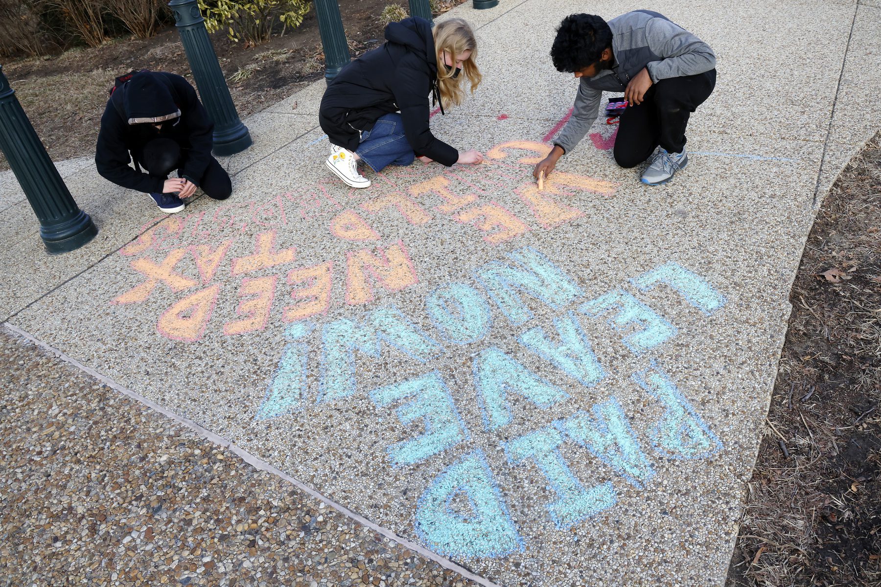 Children write on a sidewalk in blue and orange chalk to promote paid leave.