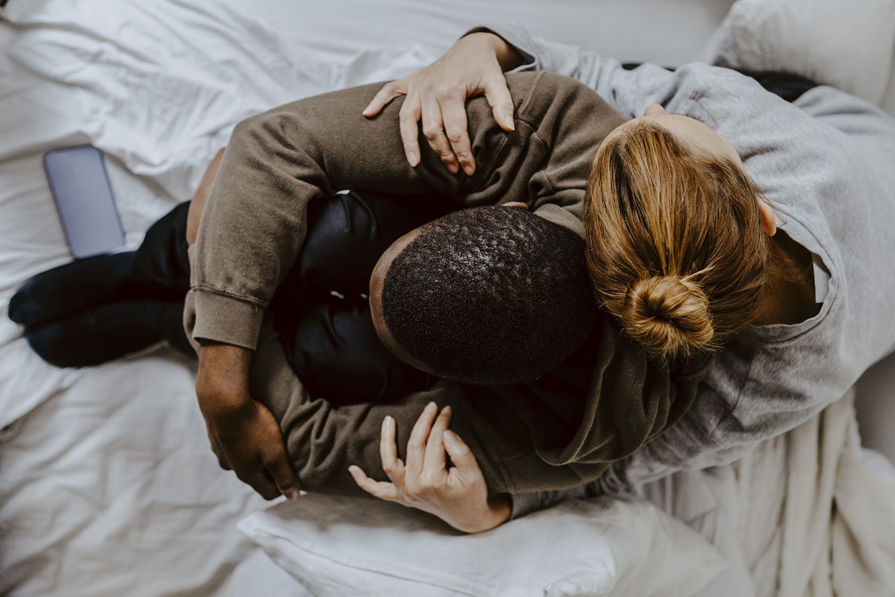 Mother embracing depressed son on bed at home.