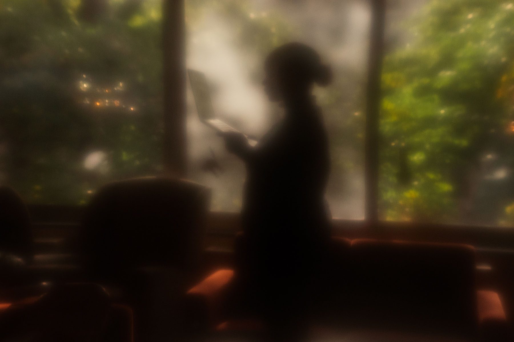 A silhouetted student stands near a window in a college dormitory holding a laptop in one hand.