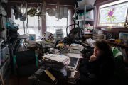 A woman sits at a busy desk. Baby seats are hung up all over the room.