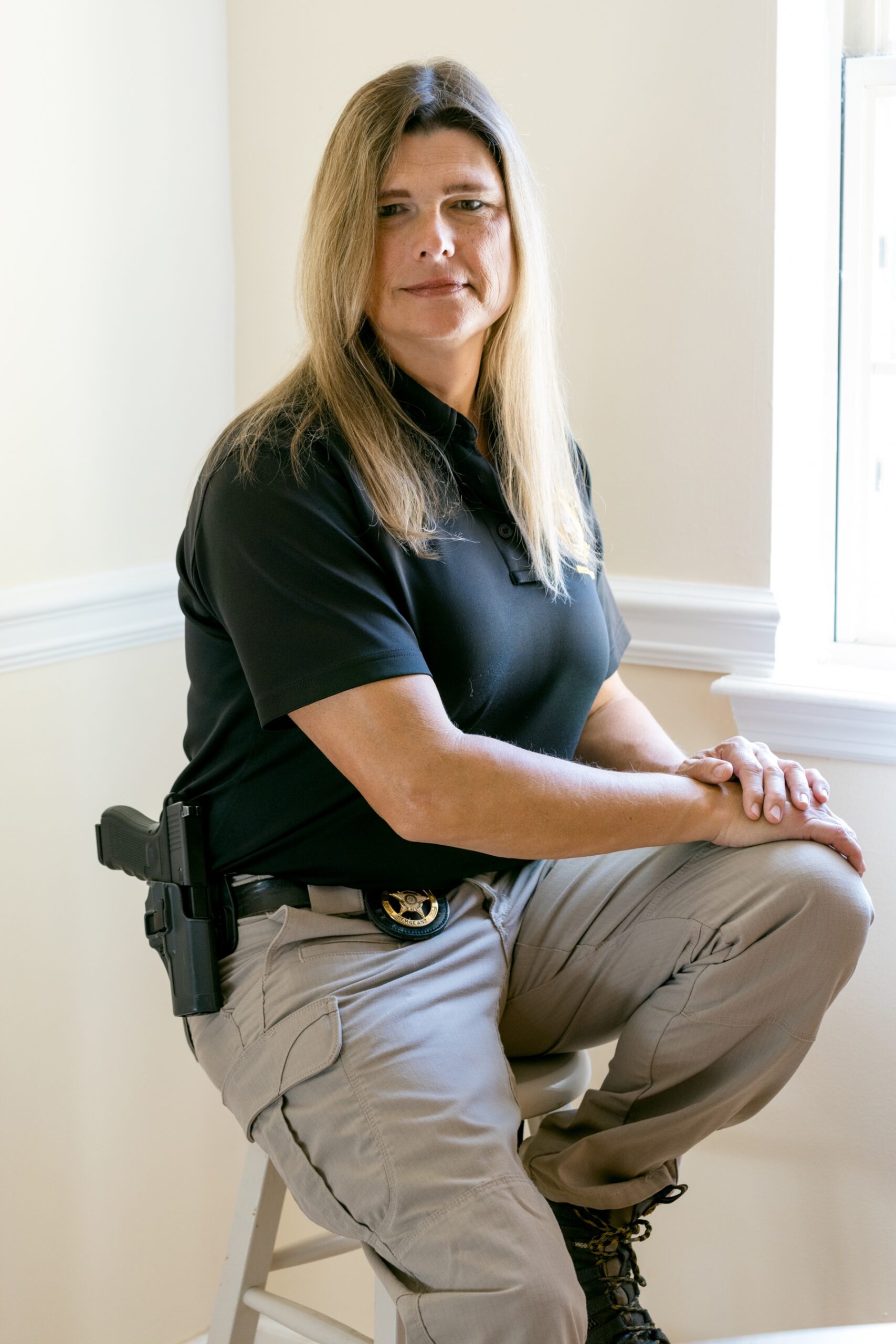 Lange sits on a barstool with one foot on the upper rung and her hands resting on her raised knee. She's in the corner of a white room.