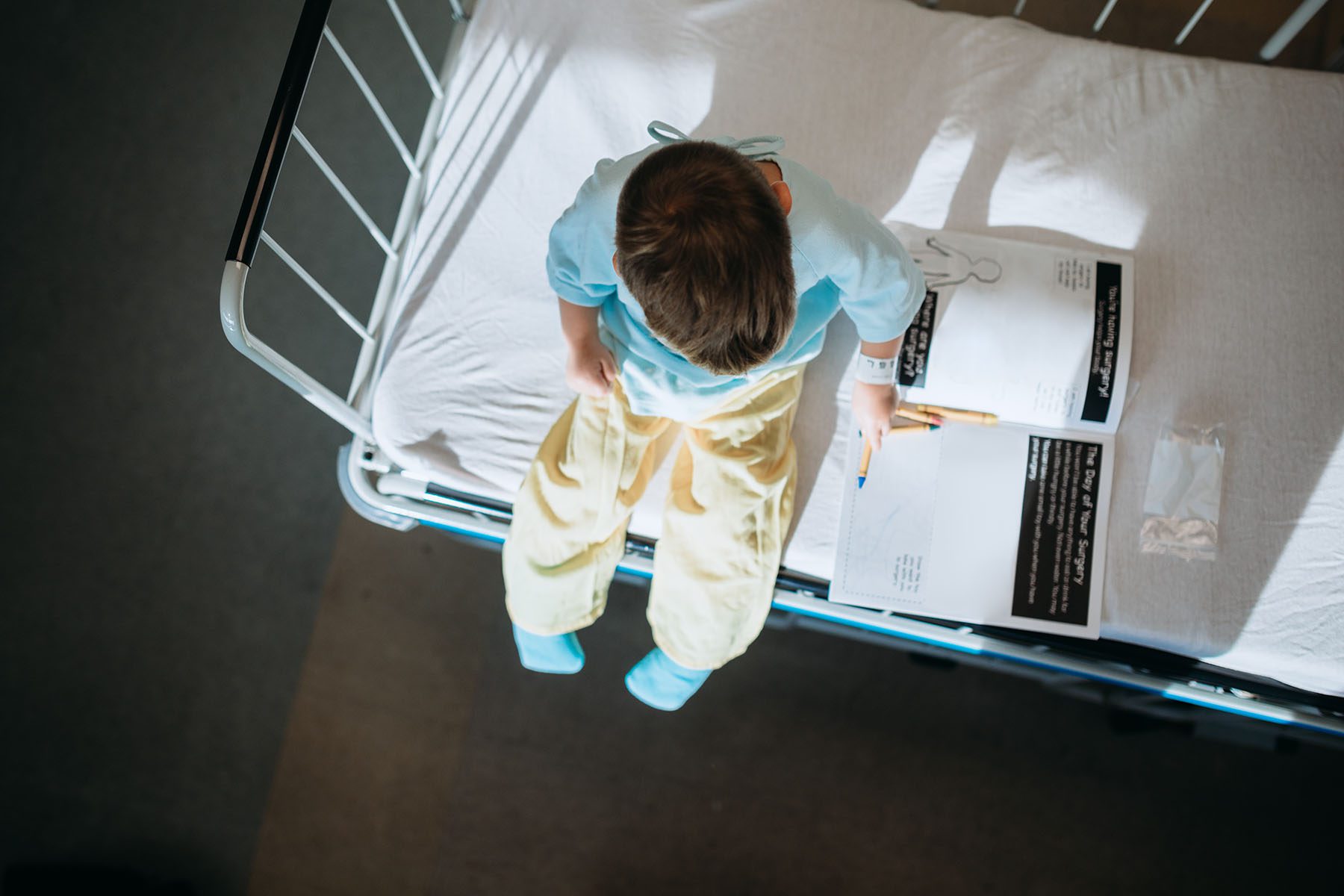 Little boy sitting on a hospital bed coloring a book.