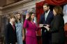 Senator Katie Britt, surrounded by her family is sworn in by Vice President Kamala Harris. Katie Britt raises her hand and smiles as her other hand is placed on a bible held by her husband. Behind her, her son and daughter are smiling.