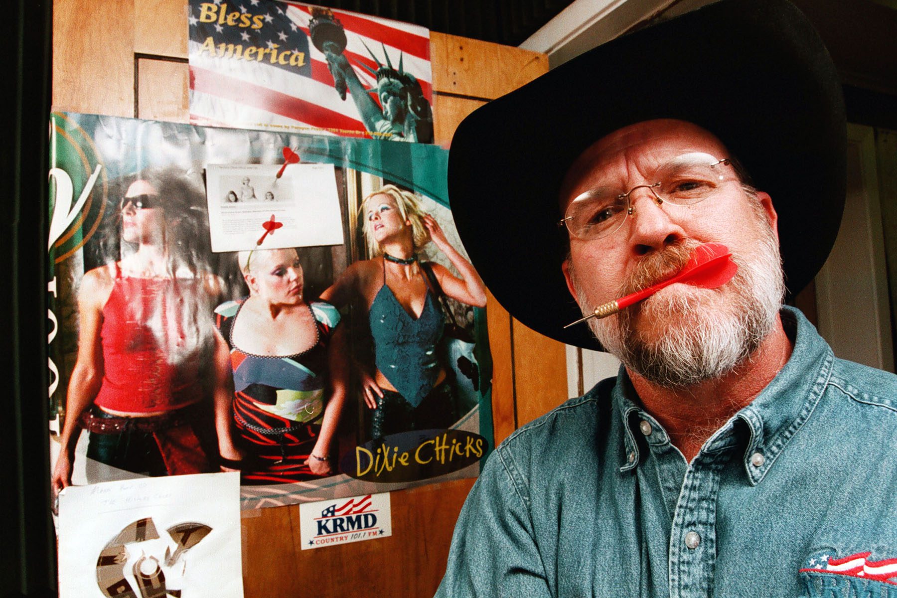 Local country radio personalities K. C. Daniels shows off the darts he has been throwing at a poster of The Chicks taped to the studio door at radio station KRMD-FM.