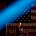 Florida Gov. Ron DeSantis speaks at a podium. A bright blue stage light passes above his head. Behind him is a large American flag.