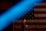 Florida Gov. Ron DeSantis speaks at a podium. A bright blue stage light passes above his head. Behind him is a large American flag.