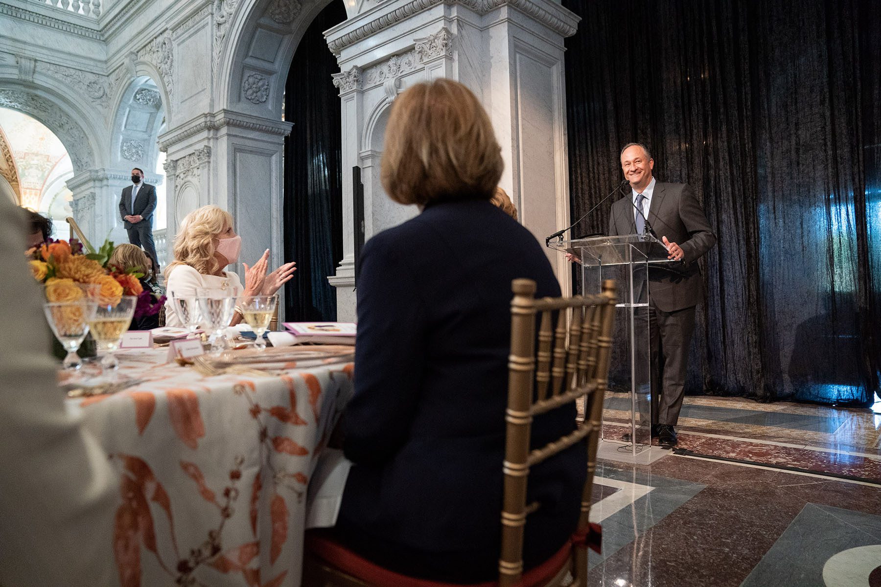 Second Gentleman Doug Emhoo stands in front of first lady Dr. Jill Biden and others and delivers a speech.