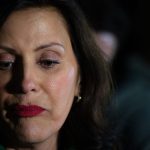 Close up of Michigan Governor Gretchen Whitmer's serious face as she listens to reporters during a news conference.