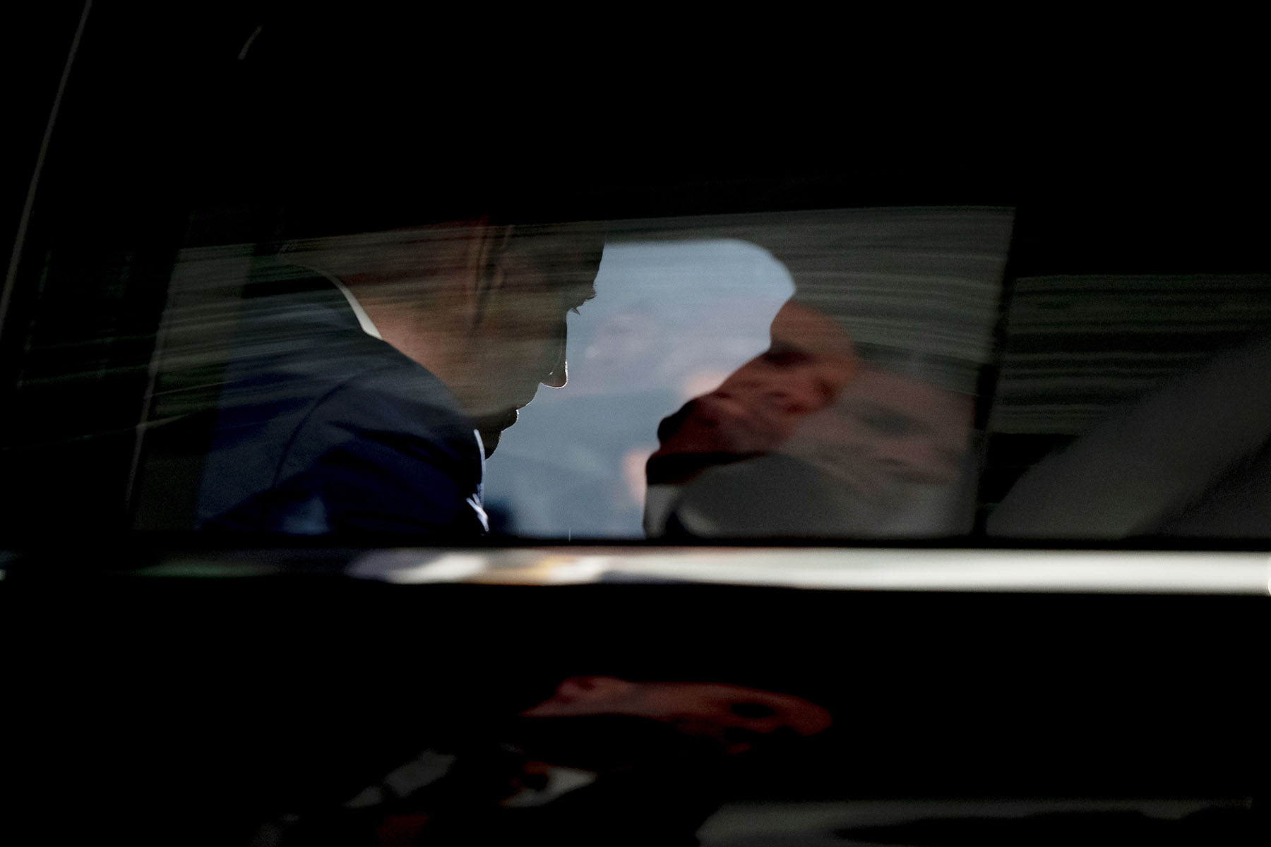 A dark image of biden seen inside the presidential limousine from outside the car's window.