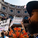 People protest with signs on the outdoor rotunda of the Texas Capitol in Austin.