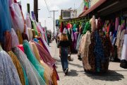 A woman walks by rolls of fabric on a sunny afternoon outside of shops in the fashion district of Los Angeles.