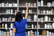 A pharmacy technician grabs a bottle of drugs off a shelve.