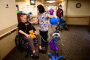 A caregiver checks a resident in a wheelchair's blood pressure in a nursing home hallway.