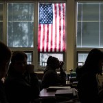 Students sit through class under a U.S. flag.