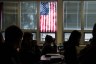 Students sit through class under a U.S. flag.