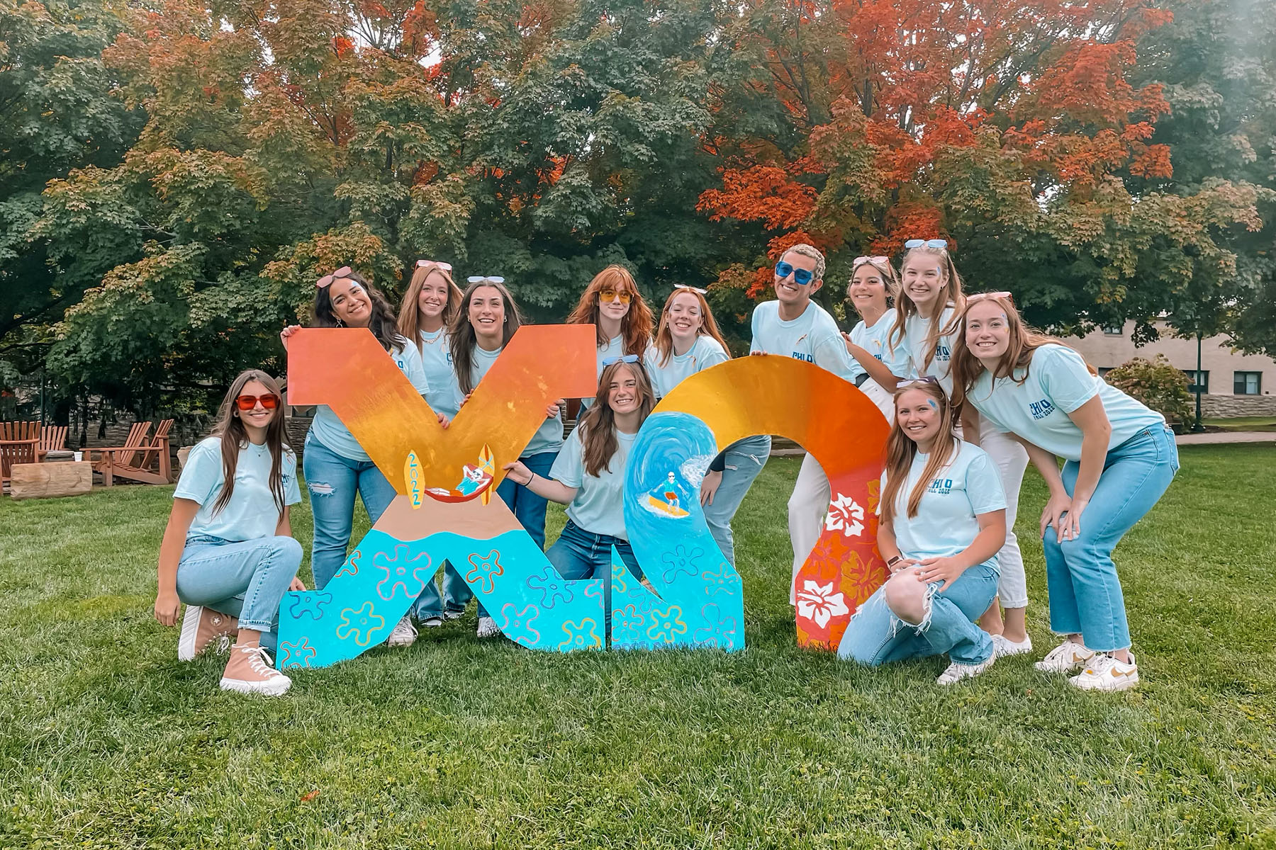 A group of people cluster around two giant Greek letters that spell out Chi Omega.