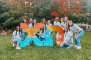 A group of people cluster around two giant Greek letters that spell out Chi Omega.