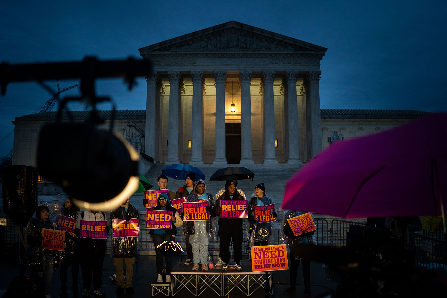 People rally in the rain to show support for the Biden administration's student debt relief plan in front of the Supreme Court.