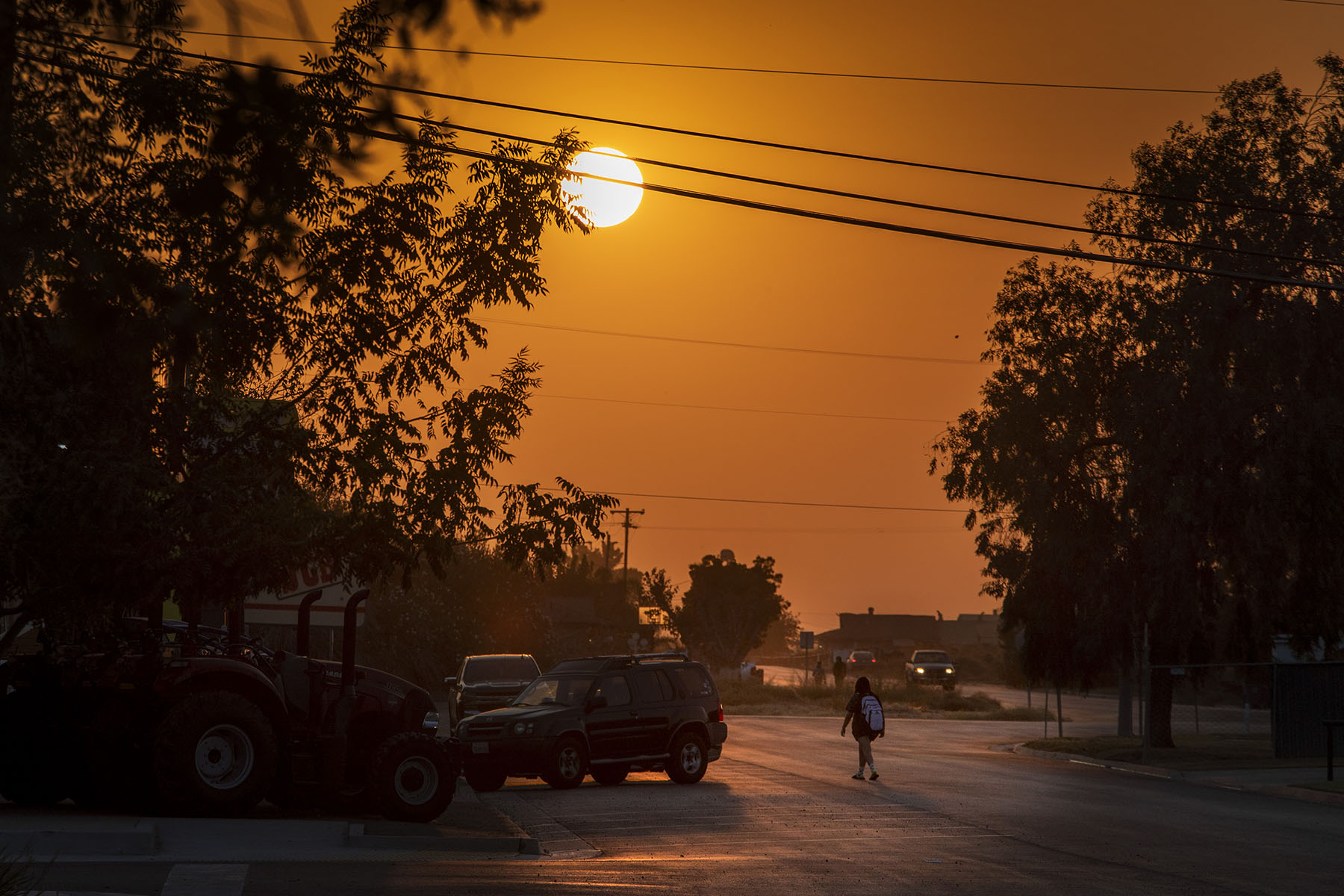 A high schooler walks towards a bus stop as the sun rises above Main St.