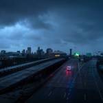 A police car drives through an empty highway as the New Orleans skyline is seen shrouded in dark clouds in the horizon.