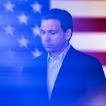 Governor Ron DeSantis speaks in front of a large american flag during a town hall event.