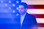 Governor Ron DeSantis speaks in front of a large american flag during a town hall event.