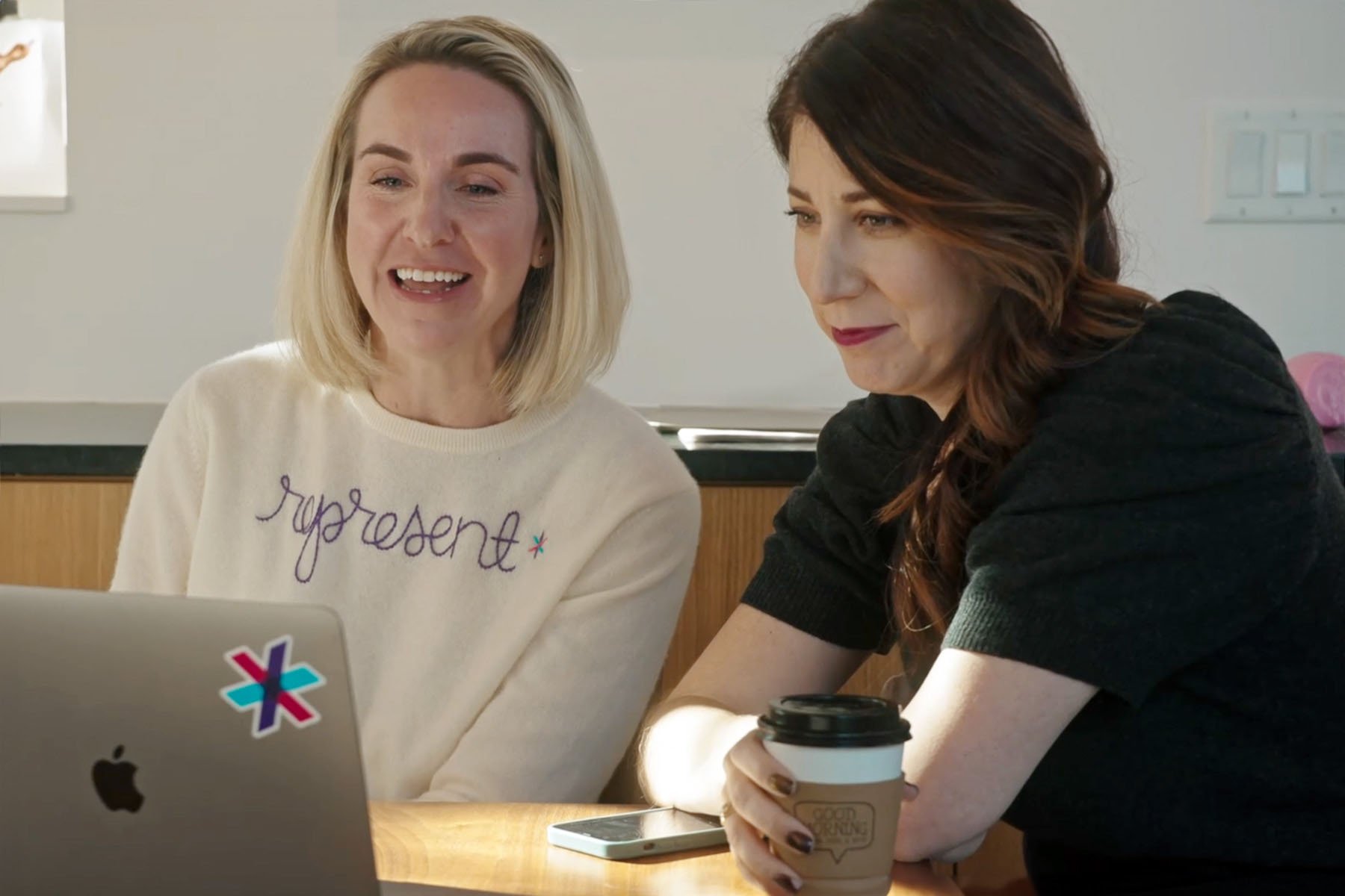 Emily Ramshaw and Amanda Zamora take a meeting together. They are both facing a laptop and smiling.