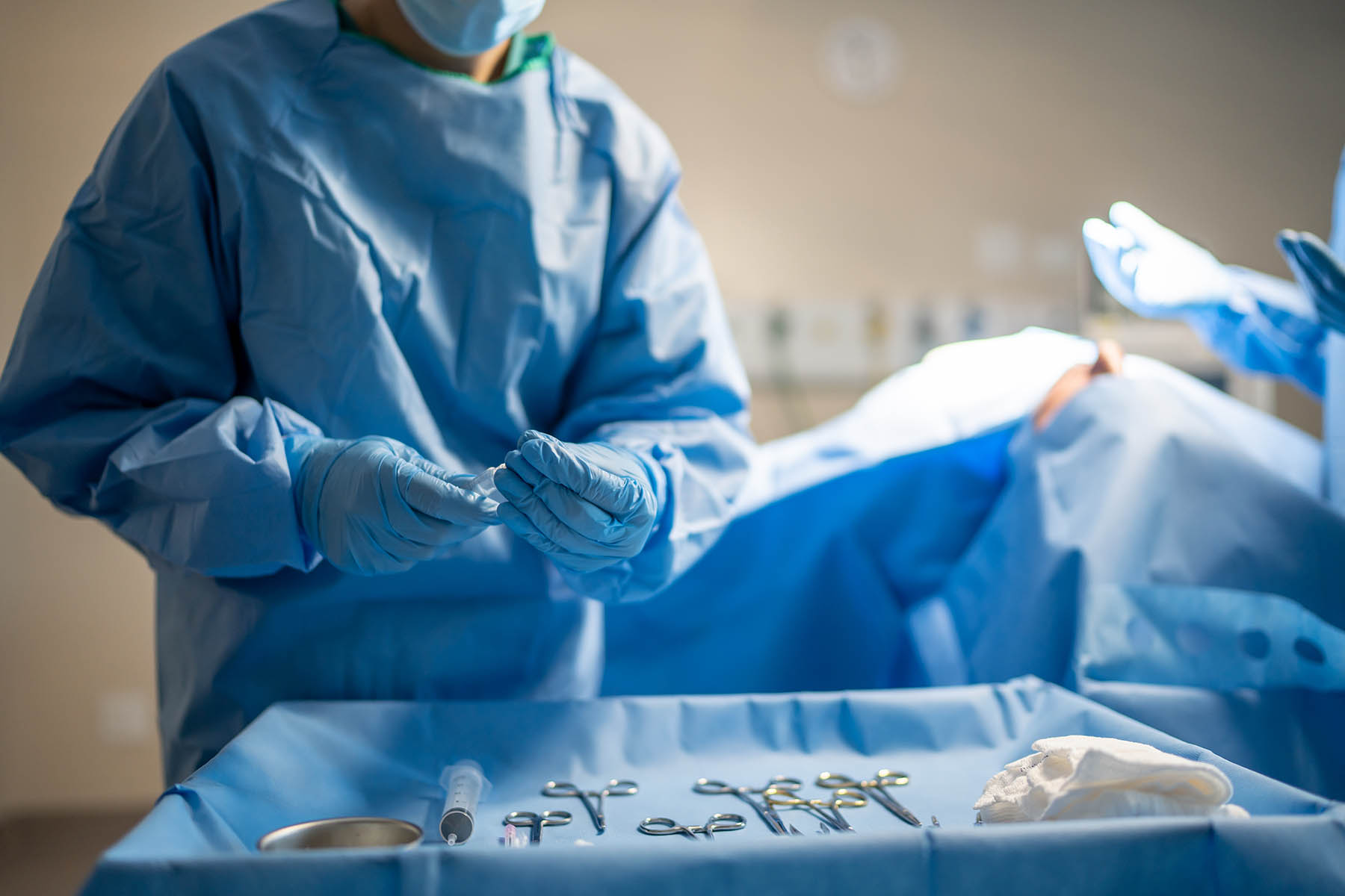 Doctor picks up a needle from a surgical instrument table.