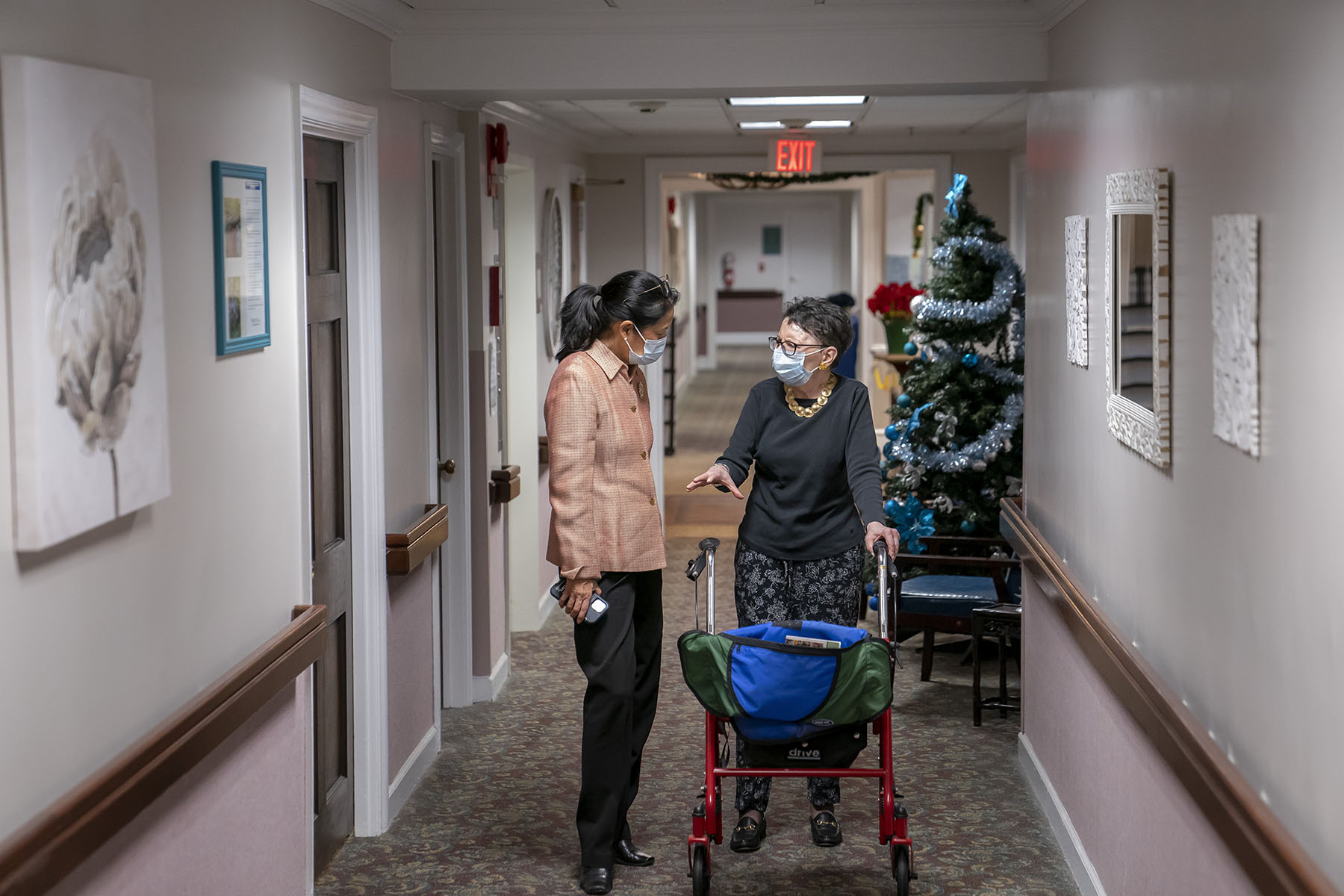 Tina Sandri, CEO of Forest Hills of DC senior living facility, left, helps a resident on walker back to her room.