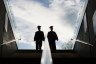 the silhouette of two college graduates in cap and gown climbing up a set of steps.