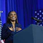 EMILY's List President Laphonza Butler speaks in front of a blue backdrop and American flags