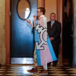 A person wrapped in a trans pride flag walks and claps.