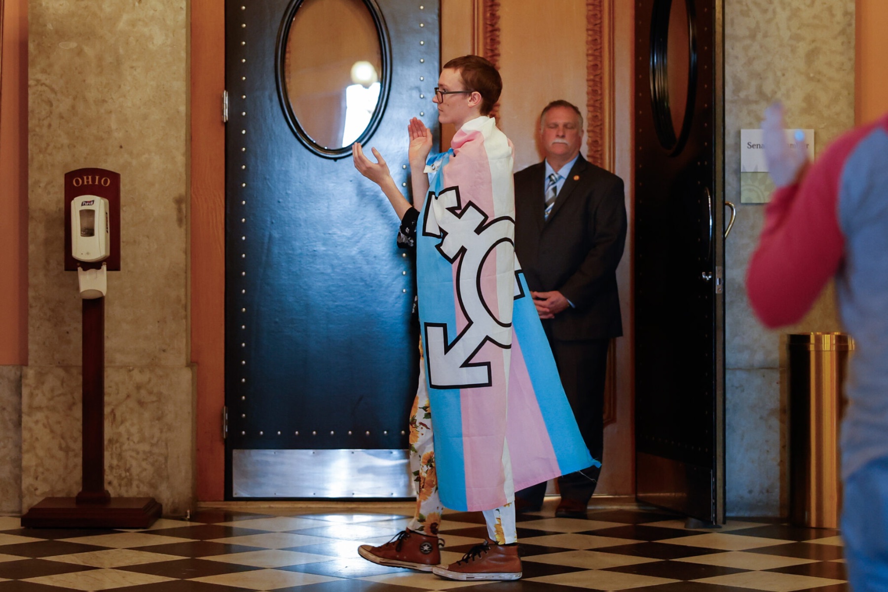 A person wrapped in a trans pride flag walks and claps.