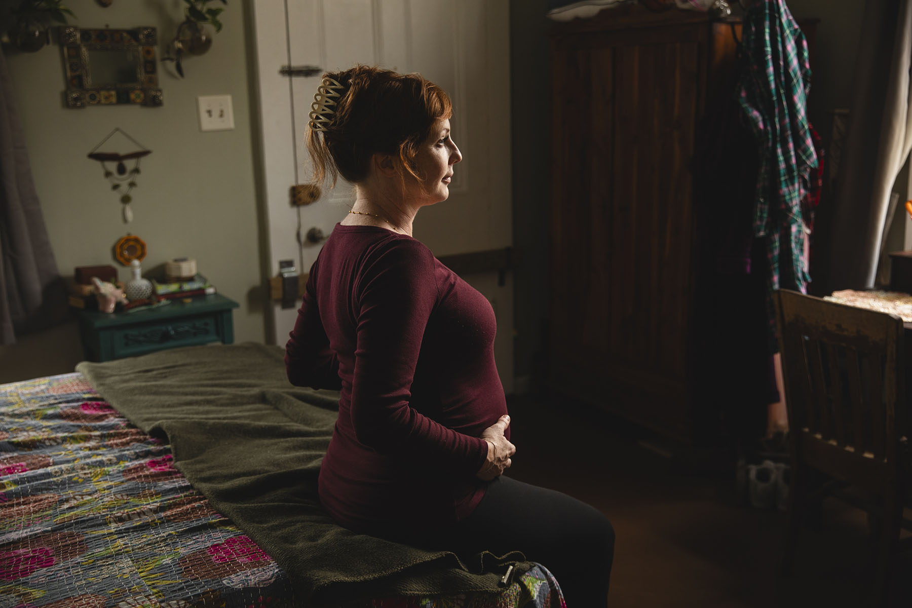 Sara Toups sits on a bed and holds her pregnant belly at her home.