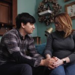 Ann Carver and her husband look at each other as they hold hands on their couch.