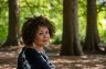 A Black woman with curly hair sits in a forest.